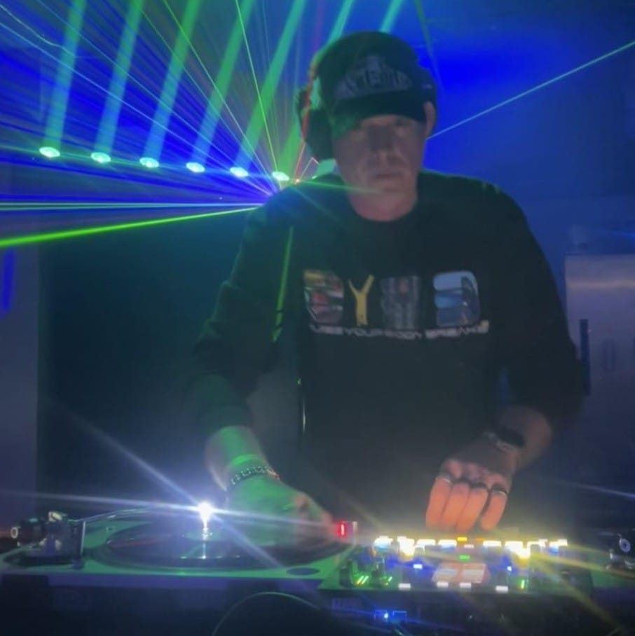 DJ Natural Nate® in BYBB shirt under intense green and blue laser beams at the mixer